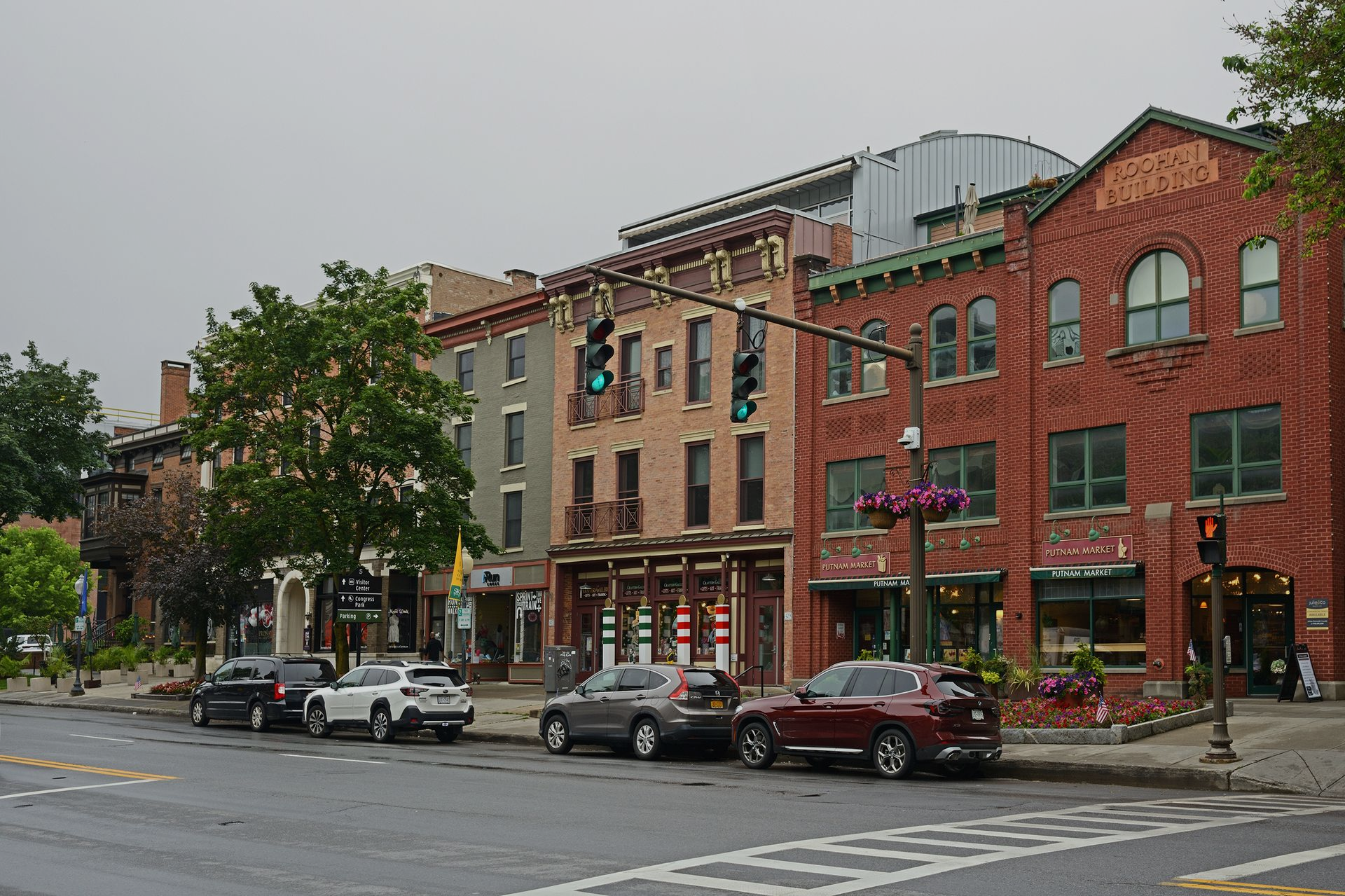 Street view of historic brick buildings with parked cars and traffic lights on a cloudy day.