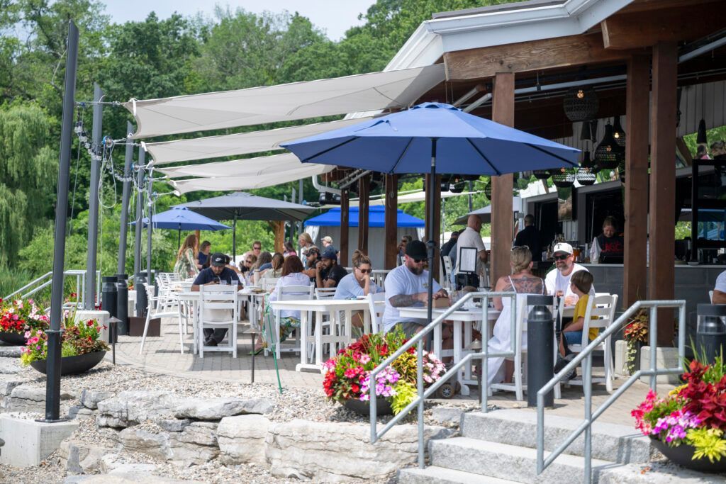 Outdoor restaurant with people seated at tables under umbrellas and a canopy.