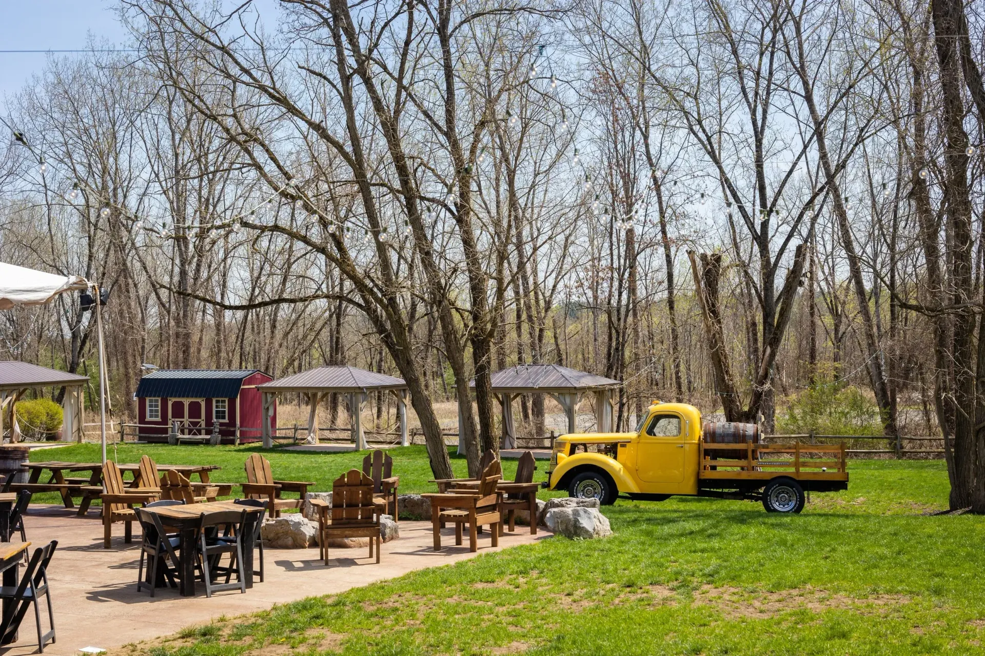 Yellow truck parked near outdoor seating area with trees and gazebos.