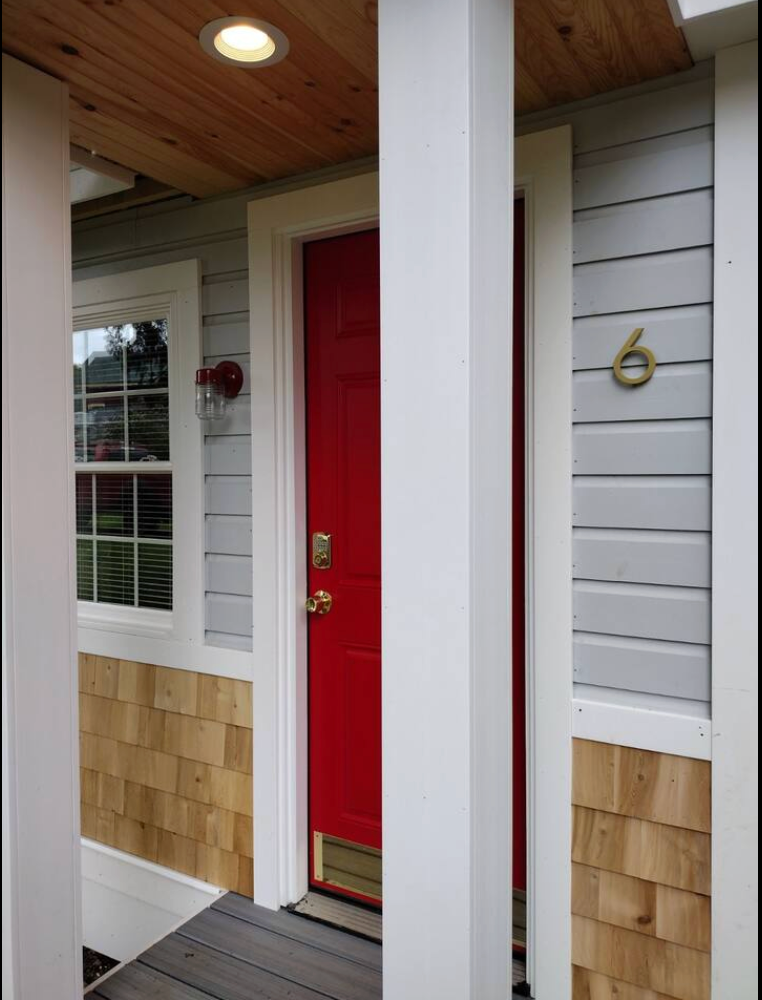 Red front door with gold number 6, light blue siding, and white pillars.