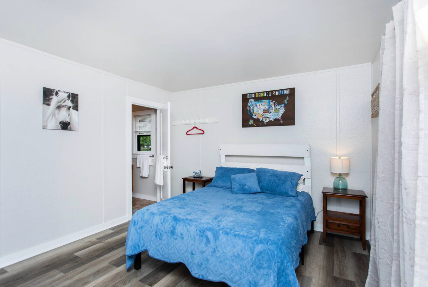 Bedroom with blue bedding, white walls, dark wood nightstands, and a door to a bathroom.