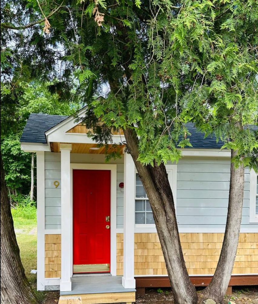 Small light blue cottage with a bright red door, cedar shake siding, and the number 9 above the door.