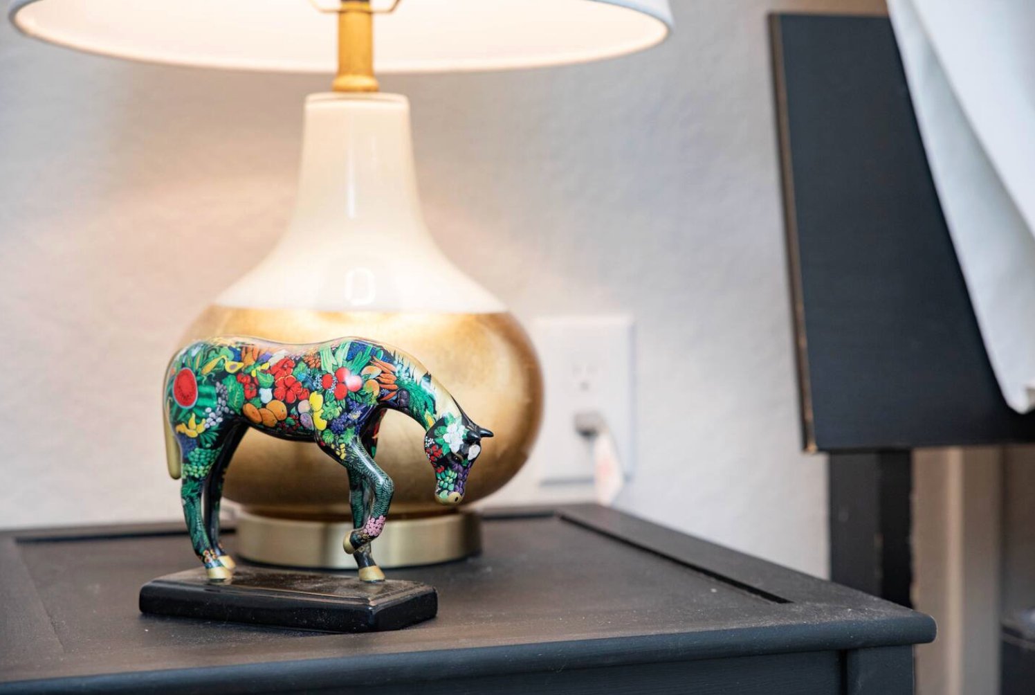 A colorful horse figurine on a black nightstand next to a lamp.