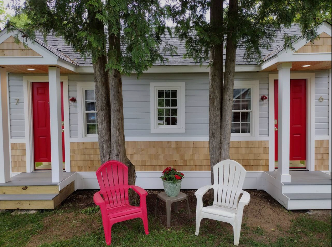 Cottages with red doors, light blue walls, and cedar shake accents. Red and white chairs sit in front.