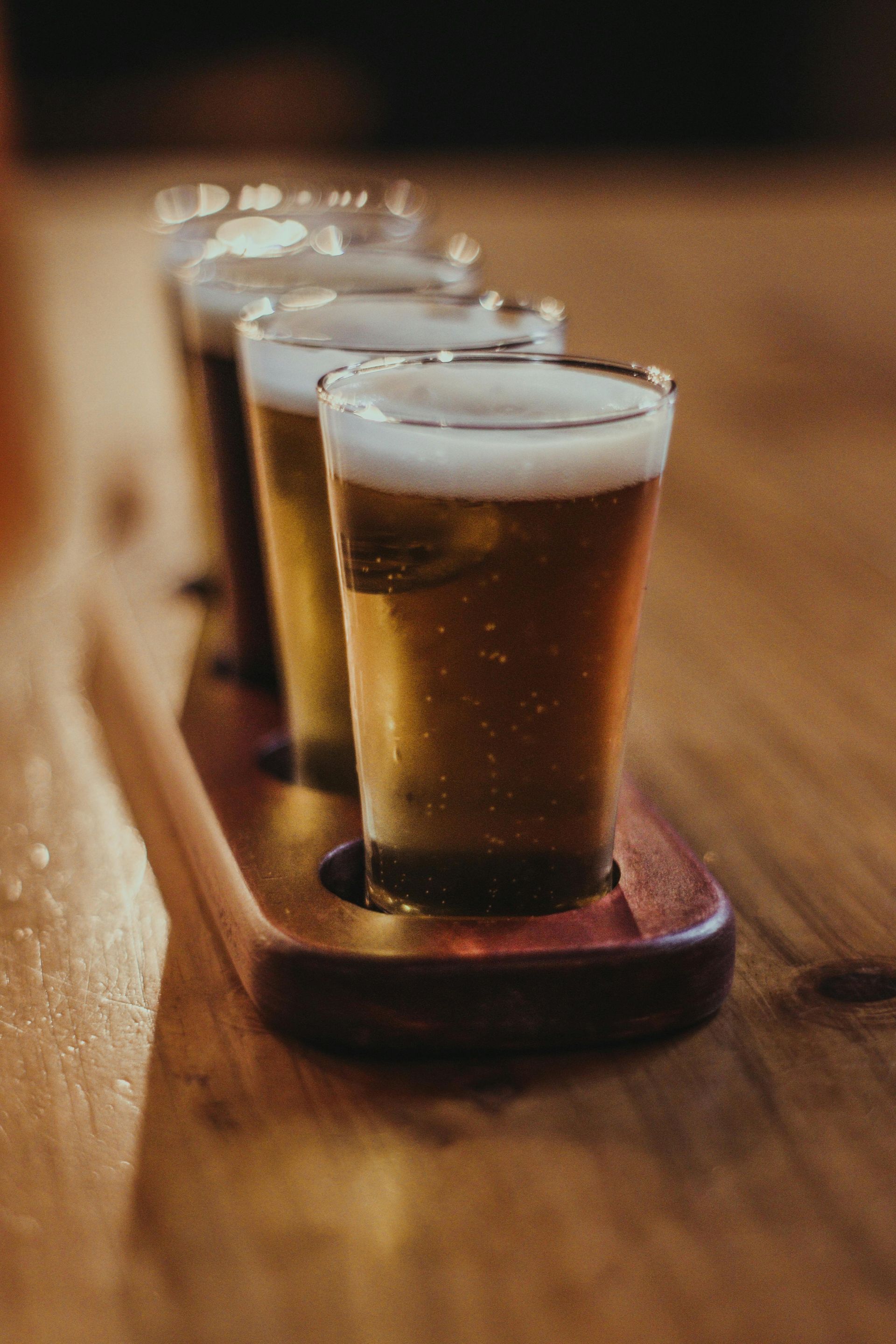 Beer flight with four small glasses of beer on a wooden tray on a table.