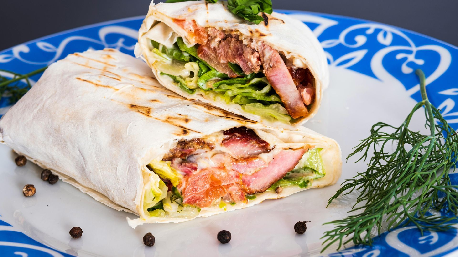 Shawarma cut in half, showcasing meat, lettuce, and sauce, on a patterned blue plate.
