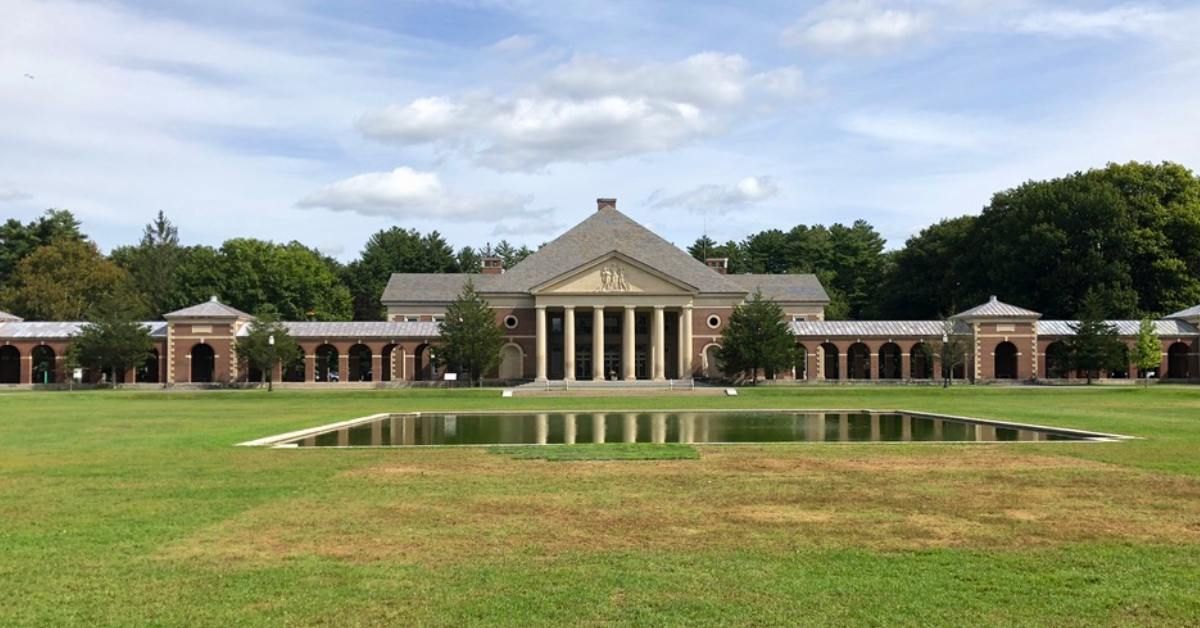 Large brick building with columns, long walkway, and reflecting pool on a grassy lawn.