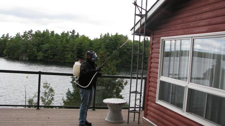 A man spraying a house with a backpack sprayer