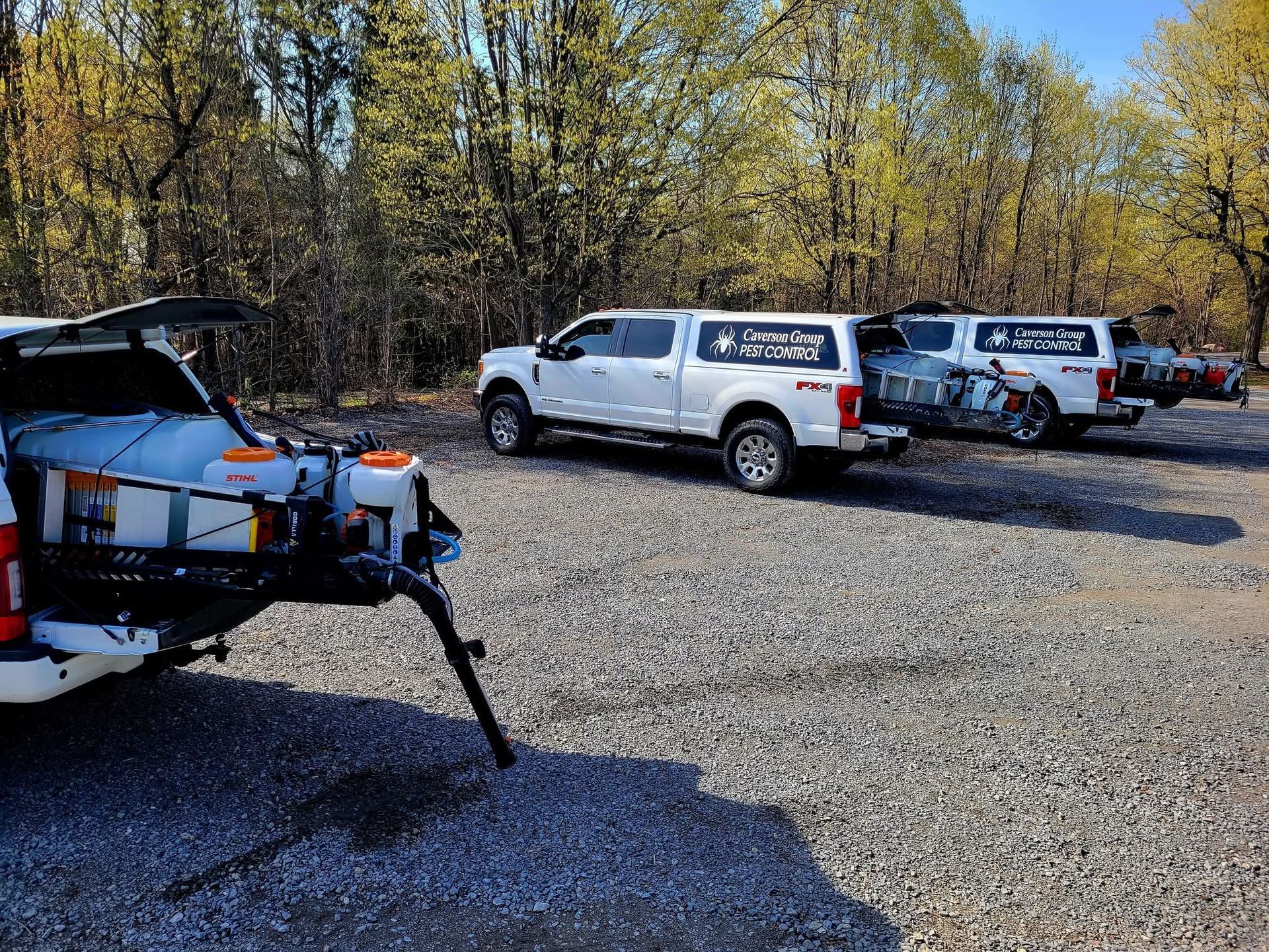 Parked SUVs on a gravel lot with a white utility trailer in the foreground and trees in back.