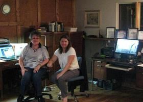 Two women are sitting in front of a computer in an office.