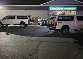 Two white trucks are parked in a parking lot in front of a building.