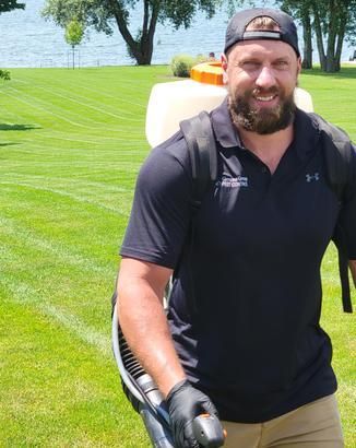 A man with a beard is carrying a backpack and a sprayer on his back.