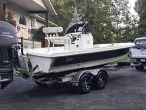 A white boat on a trailer is parked in front of a house.