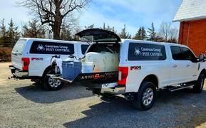 Two white utility trucks parked beside an open vehicle trunk in a lot