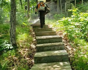 A man is spraying insecticide on a set of stairs in the woods.