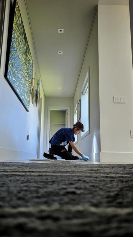 A man is kneeling down in a hallway cleaning the floor.