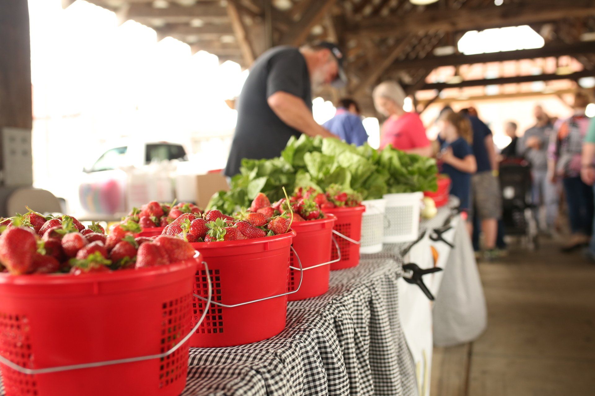 a row of red buckets filled with strawberries are on a table at a farmers market
