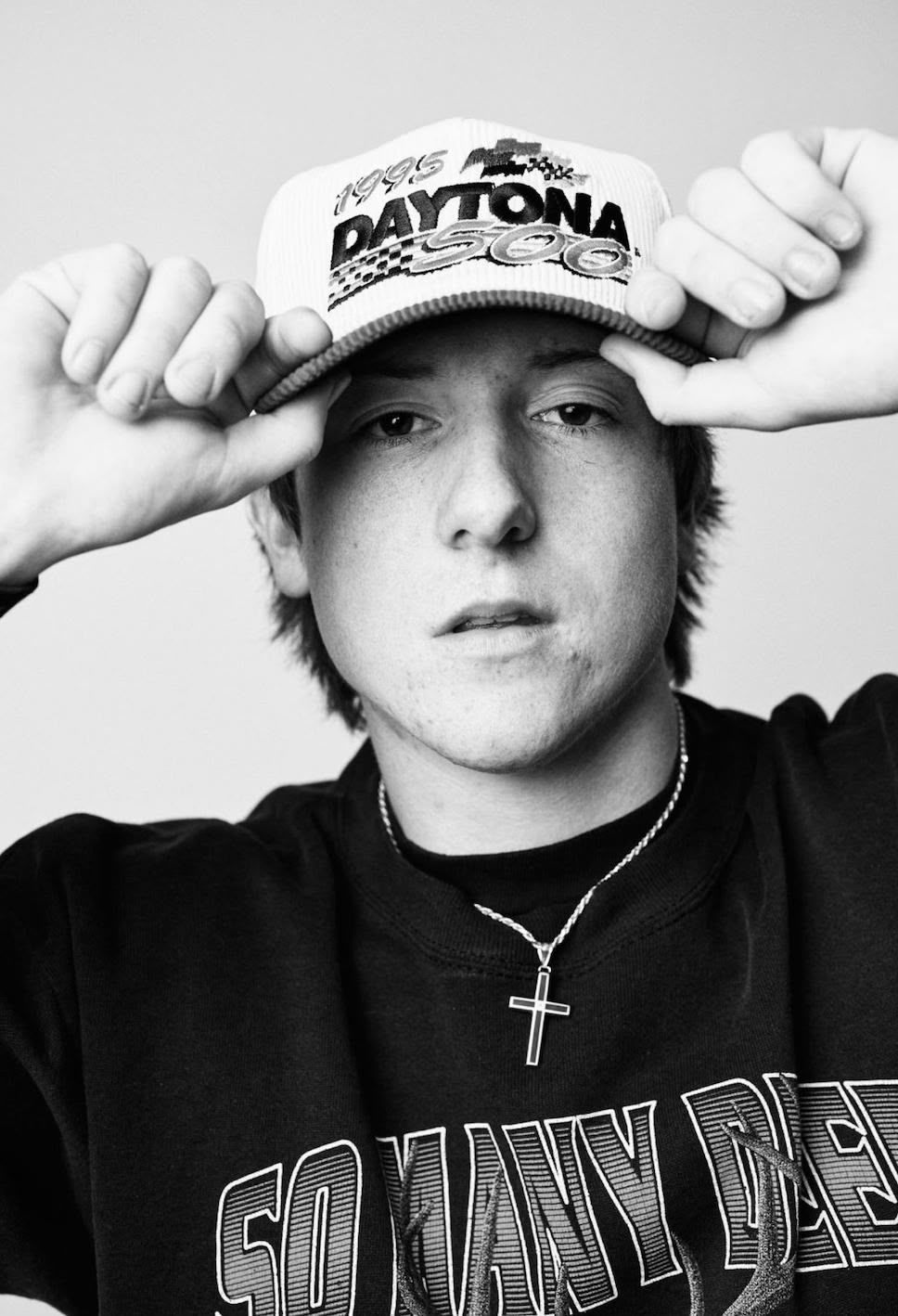 A black and white photo of a young man wearing a daytona hat
