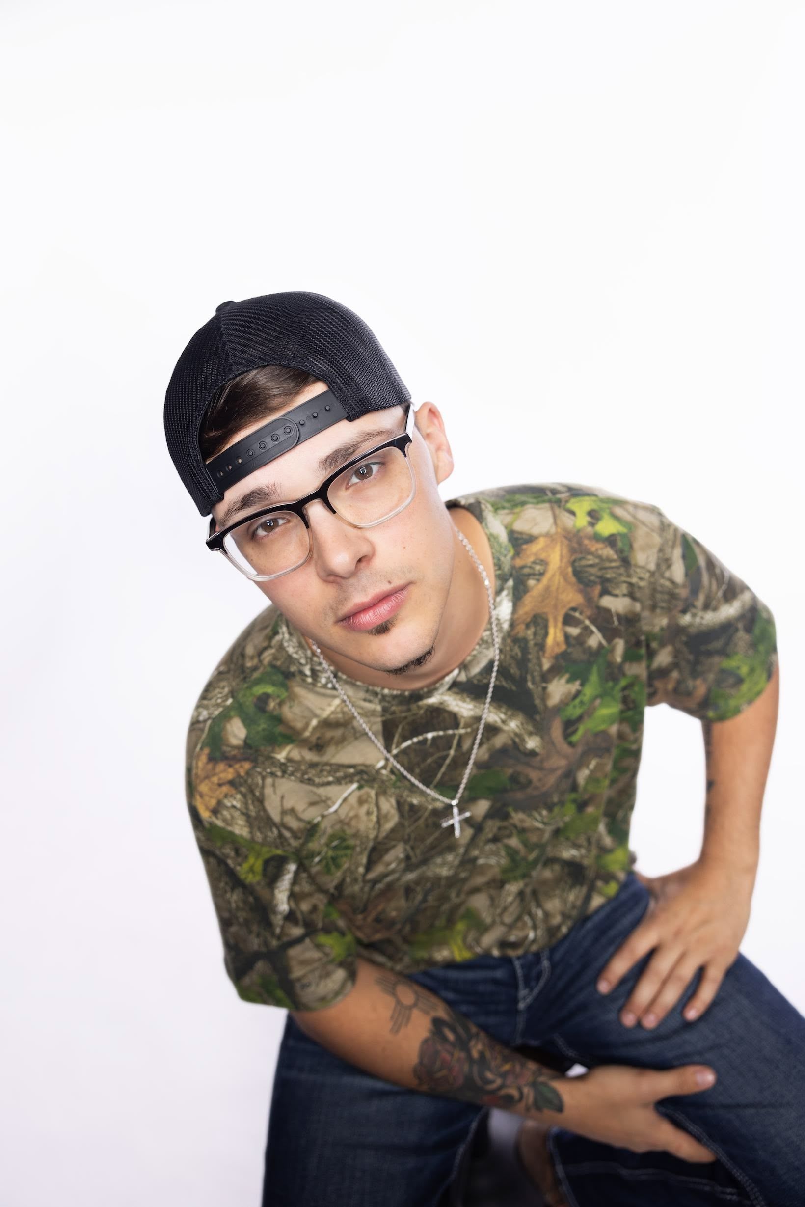 A man wearing glasses and a hat is kneeling down with his hands on his hips.