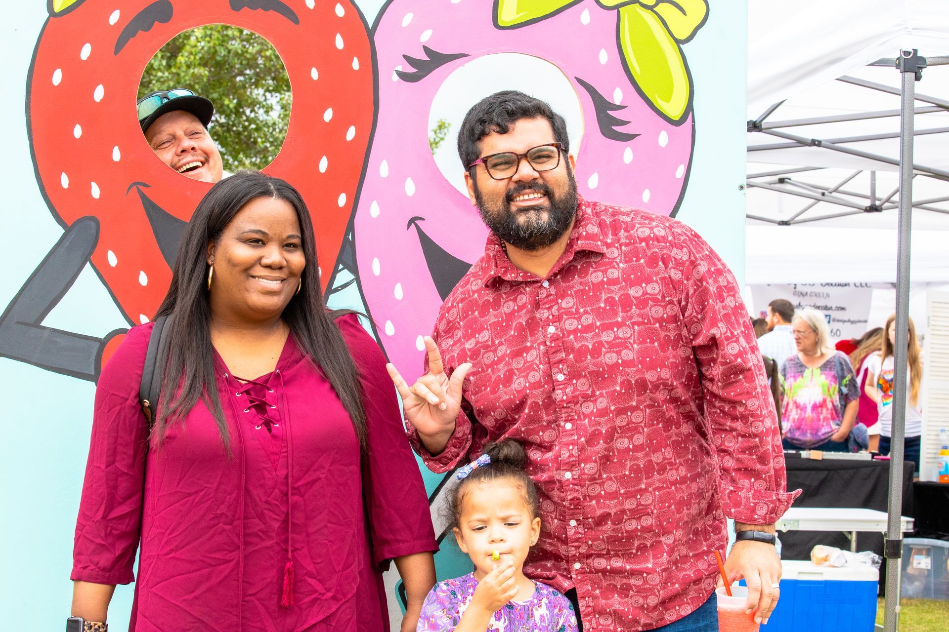 a man , woman and child are posing for a picture in front of a strawberry mural .
