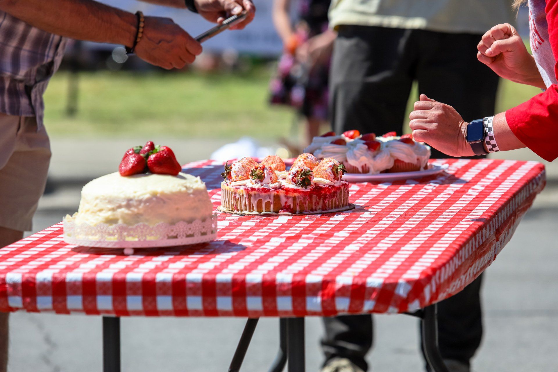 a person is cutting a cake on a table with a red and white checkered tablecloth .