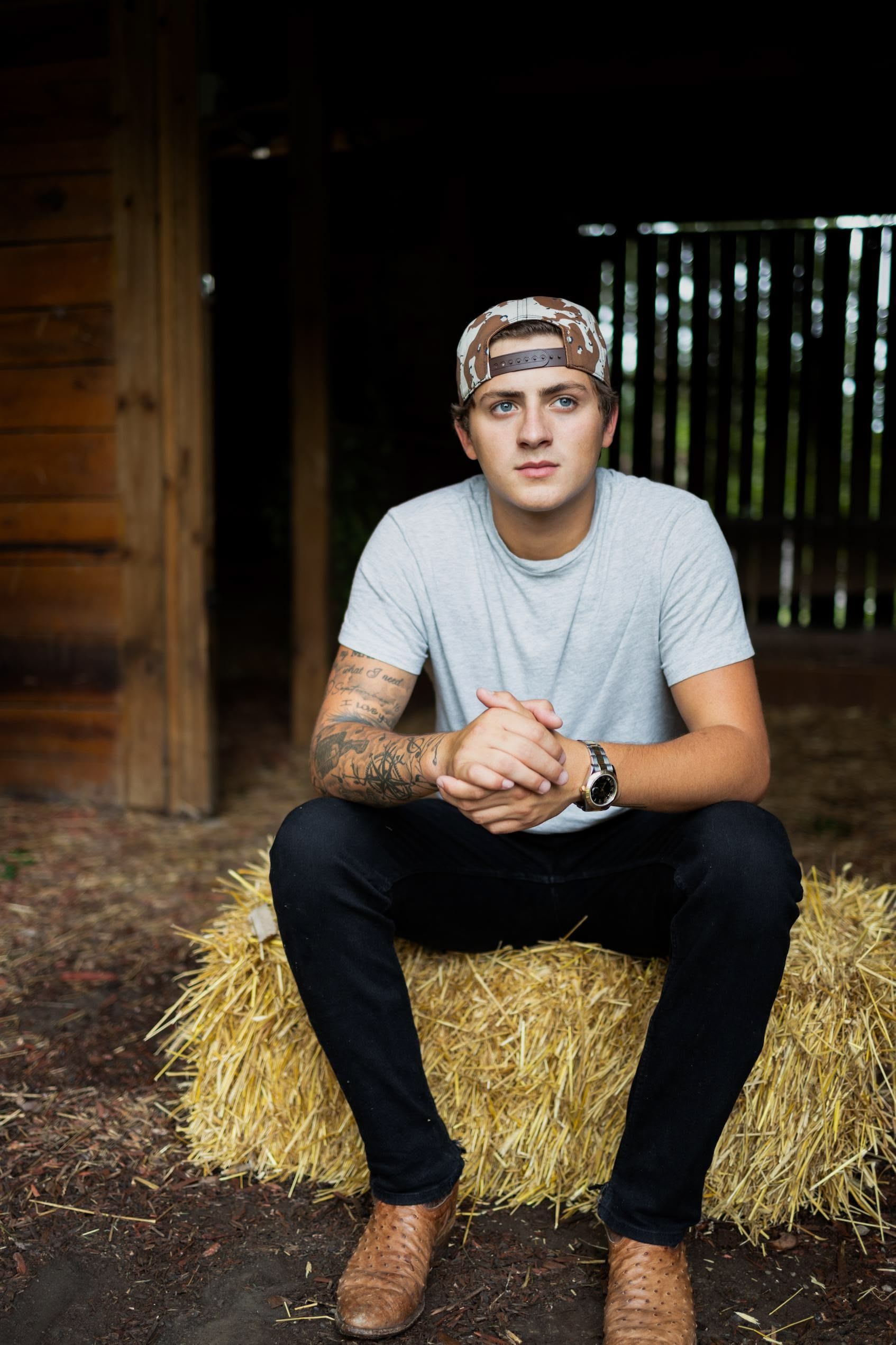 A young man is sitting on a bale of hay.