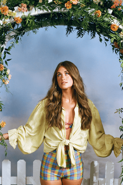 A woman in a yellow dress is standing in front of a wooden wall.