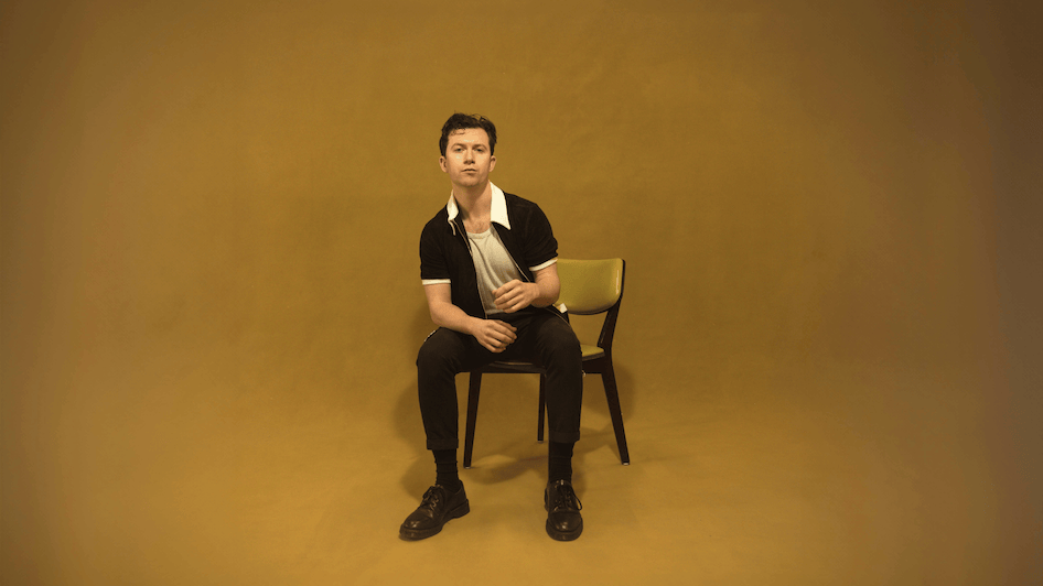 A man wearing glasses and a hat is kneeling down with his hands on his hips.