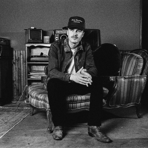 A young man is sitting on a bale of hay.