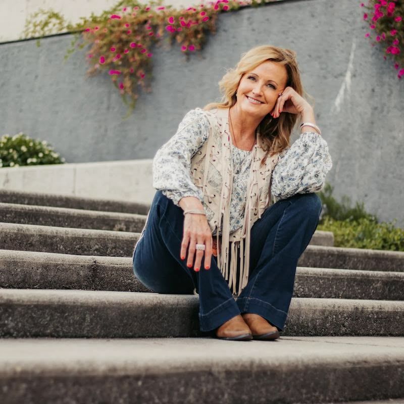 A woman in a yellow dress is standing in front of a wooden wall.