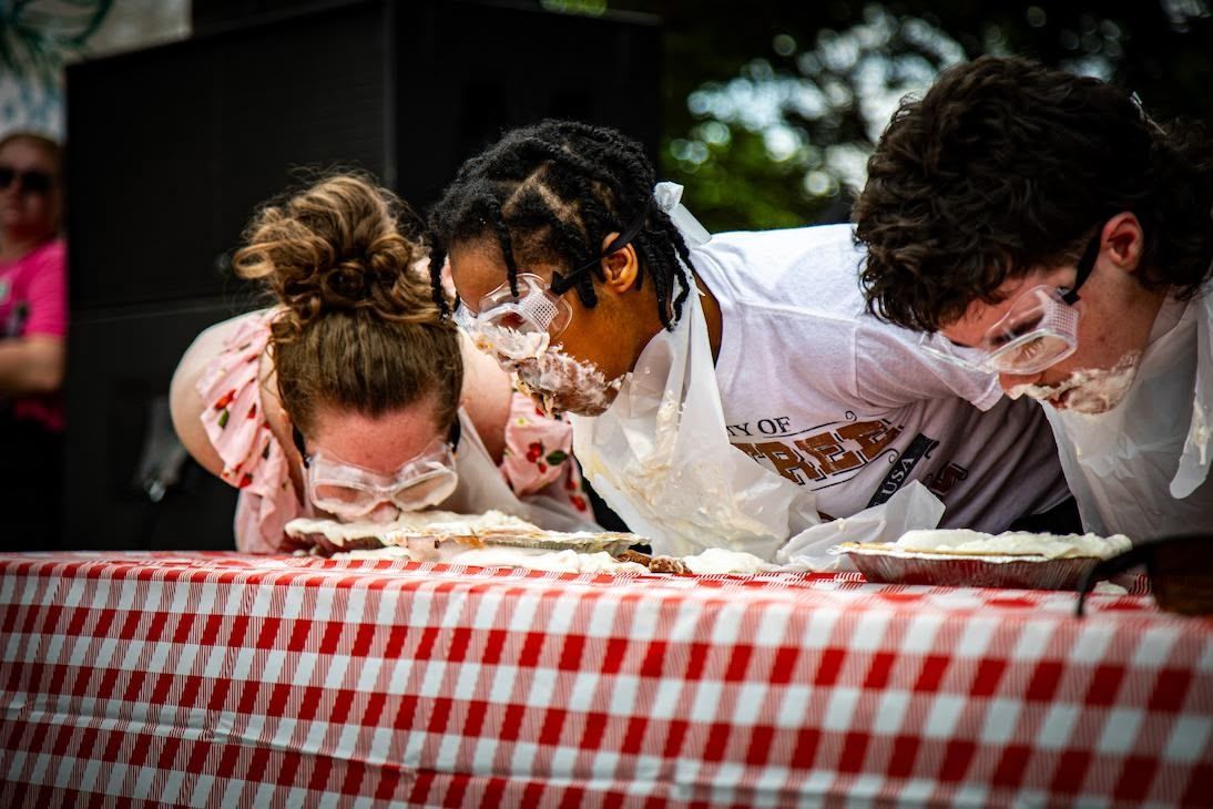 A person is cutting a cake on a table with a checkered tablecloth.