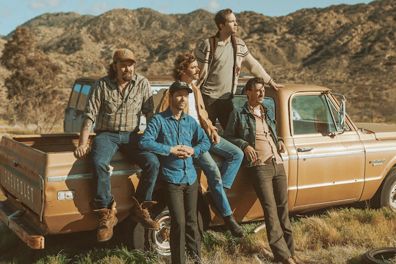 A woman in a yellow dress is standing in front of a wooden wall.