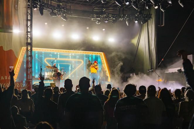A group of people are sitting in front of a stage with a neon sign that says aston corbin.