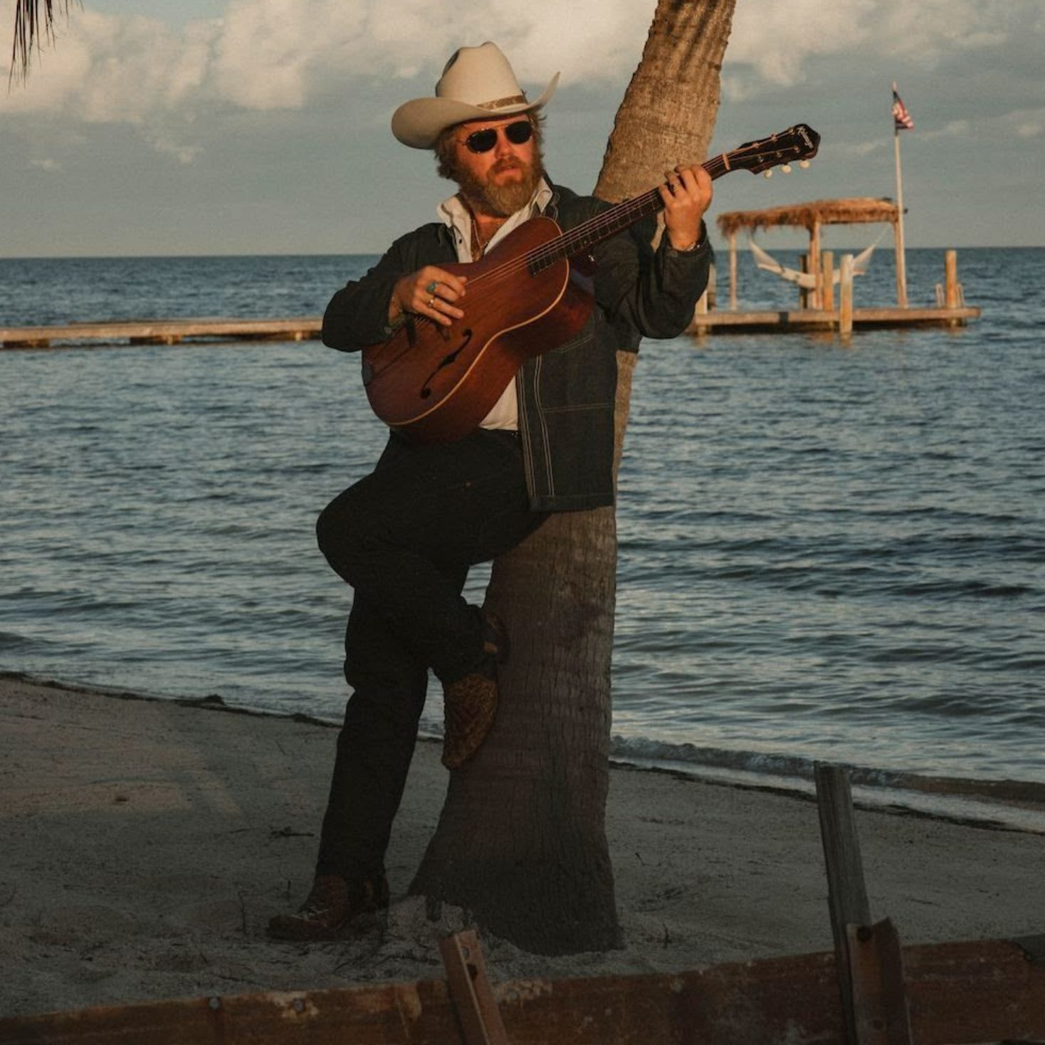 A man wearing a red hat and a white t-shirt is standing with his arms crossed.