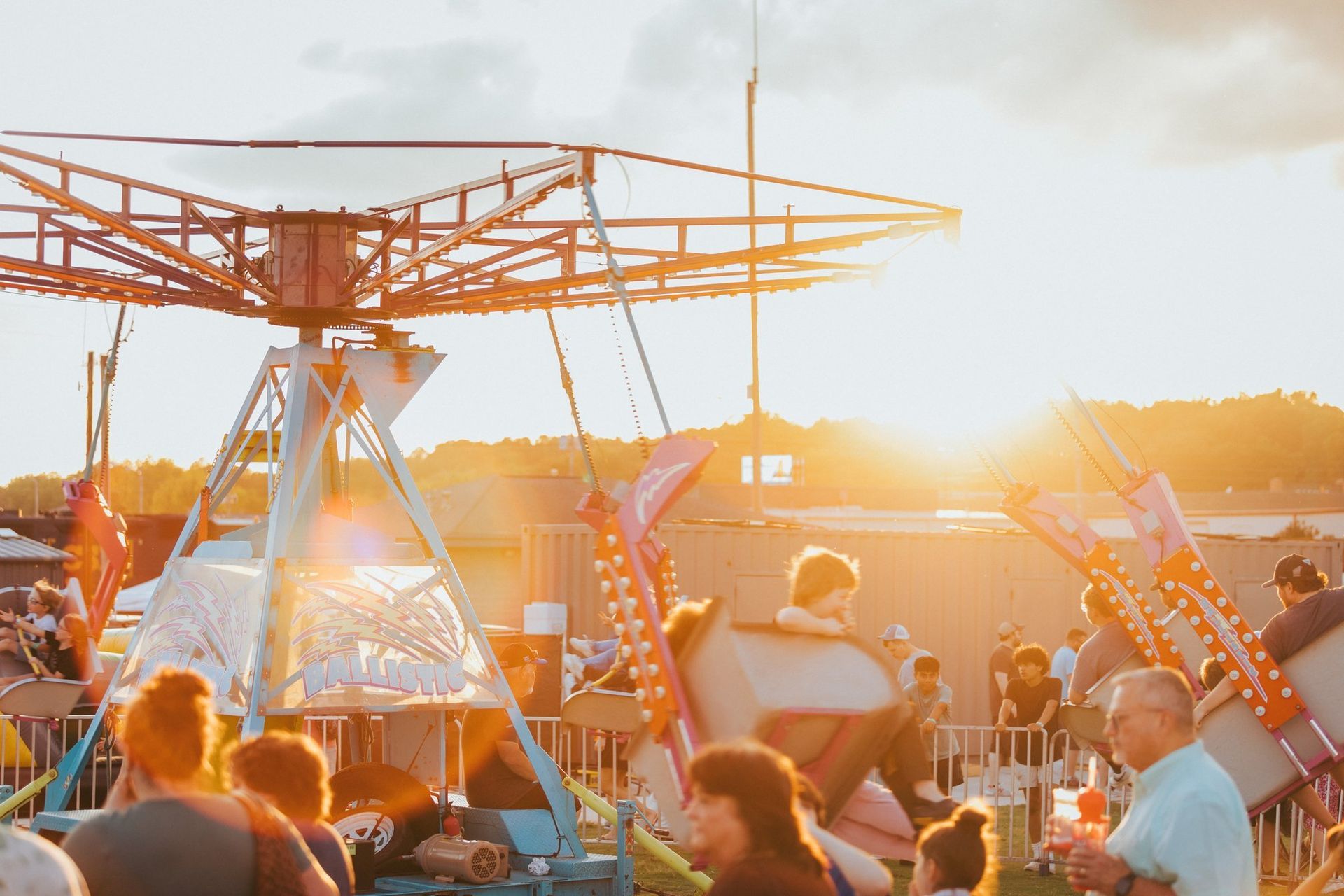 People riding a swing carousel at a fairground during a bright, golden sunset.