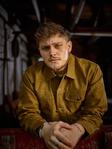 Silhouette of a person playing a drum kit. Cyan figure on an orange background, raising drumsticks.