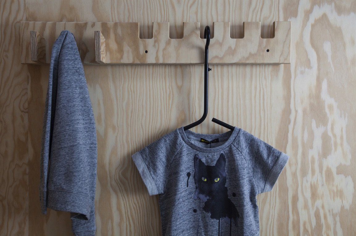 a gray shirt with a black cat on it is hanging on a wooden rack .