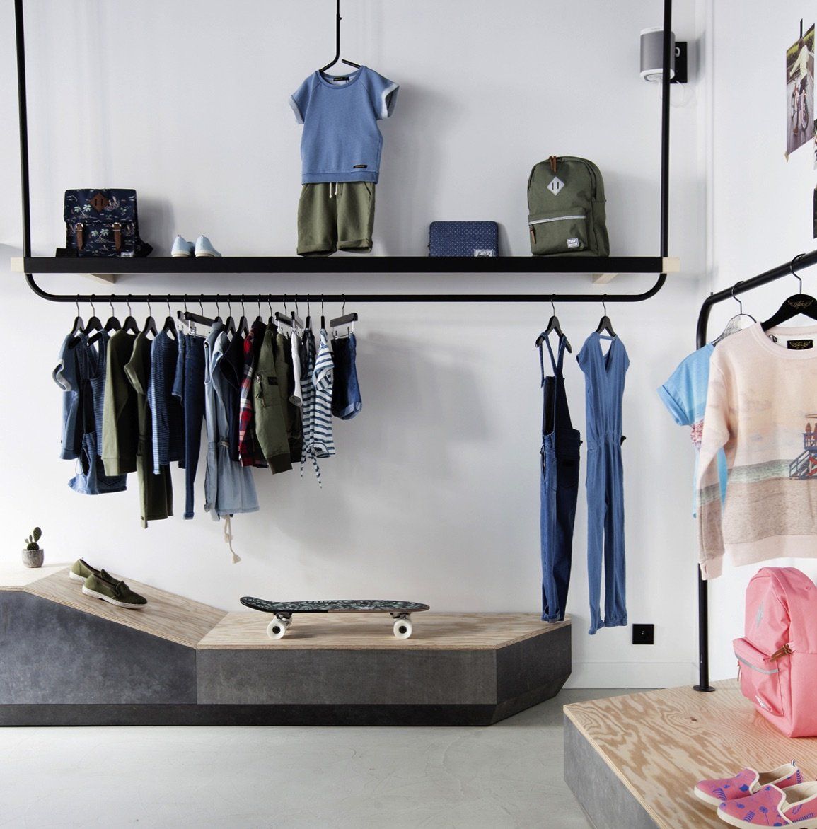 clothes hanging on a rack in a store with a skateboard on the floor
