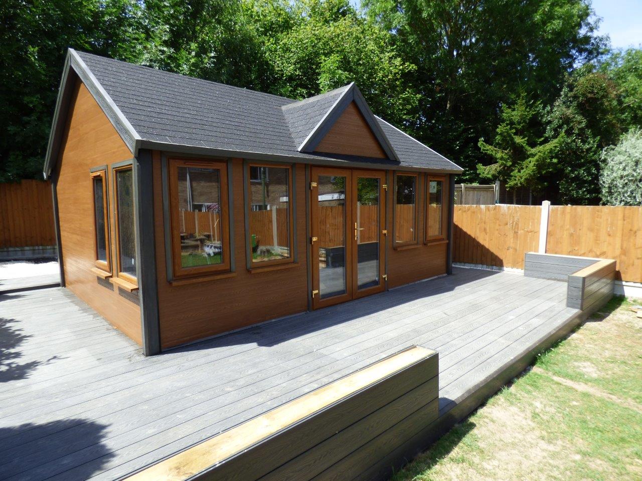 a small brown house with a black roof and a wooden deck