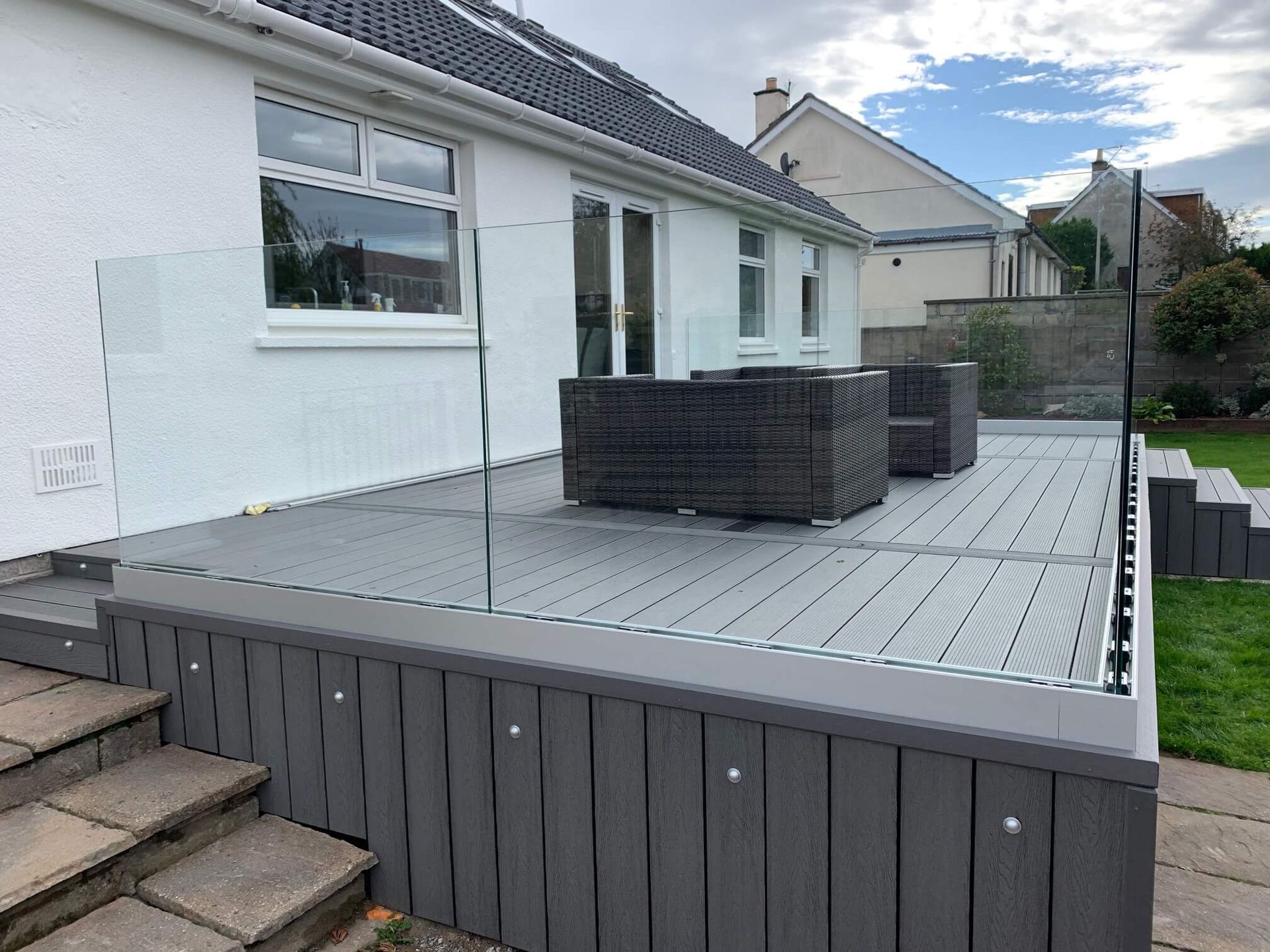 a patio with a glass railing and chairs on it in front of a house .