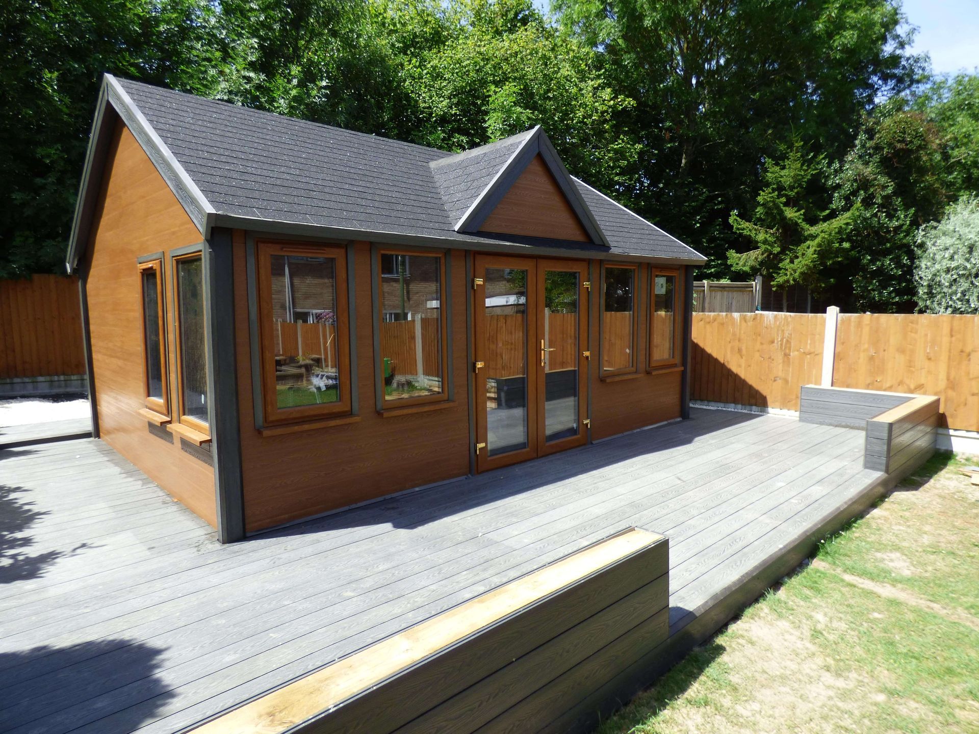a small brown house with a black roof is surrounded by trees and a wooden fence .