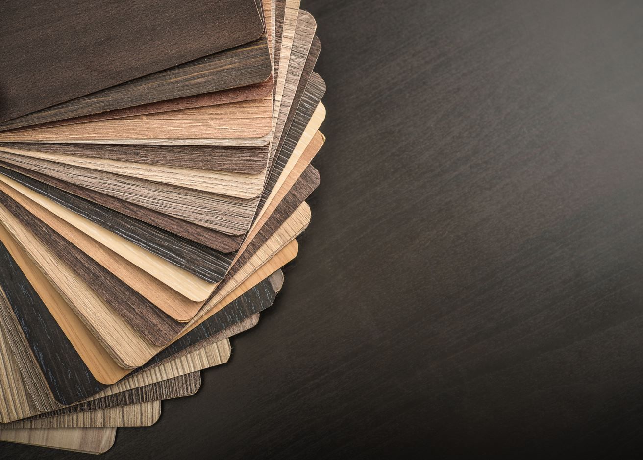 A stack of different types of veneered plywood panel samples on a black table.