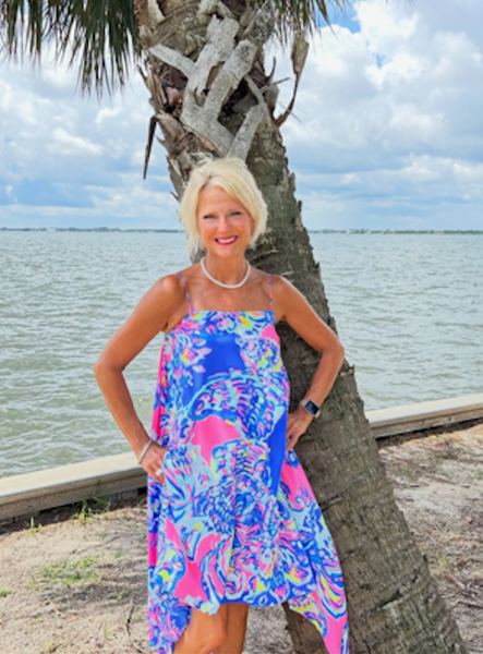 Patti Quiroz a woman in a pink jumpsuit stands in front of a wrought iron door
