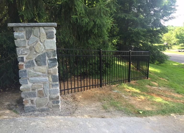 There is a stone pillar next to a metal fence.