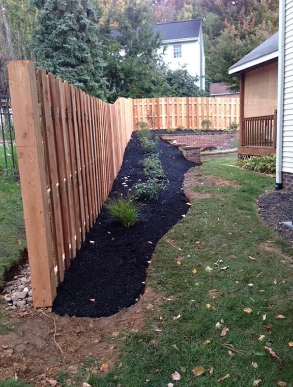 A wooden fence is surrounded by black mulch in a backyard