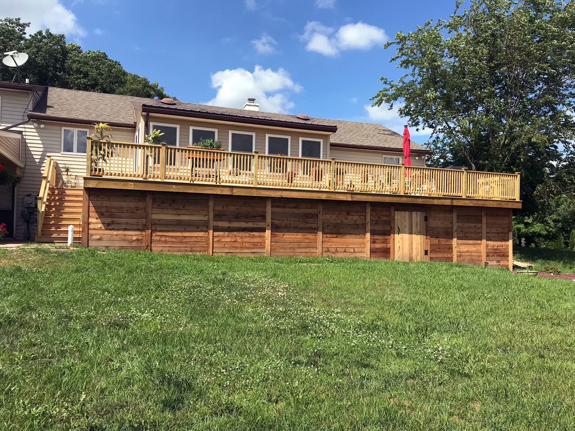 A large wooden deck is sitting on top of a lush green field in front of a house.