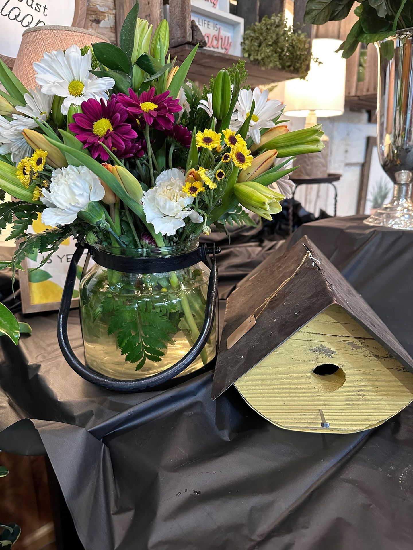 A vase filled with flowers is sitting on a table next to a birdhouse.