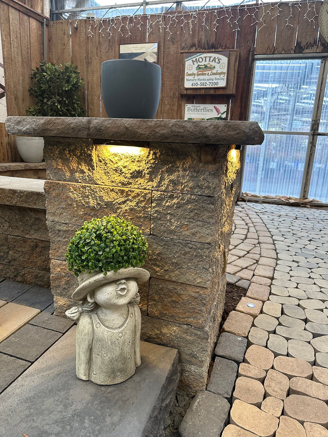 A statue of a woman in a hat is sitting on a brick wall.