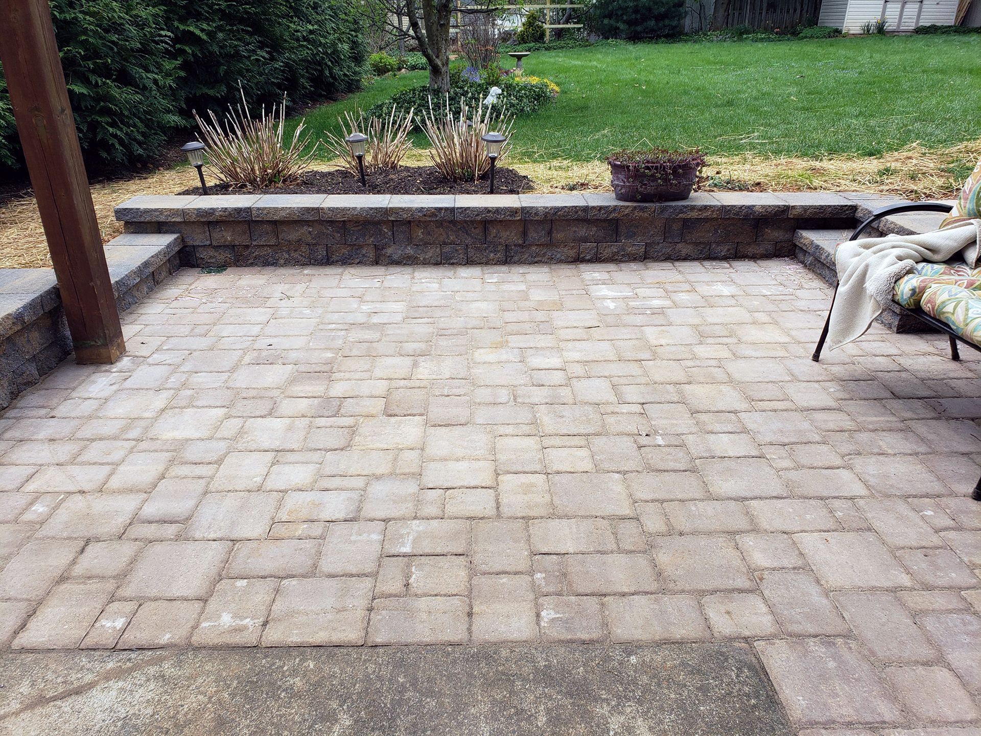 A brick patio with a chair and a wall in the backyard.