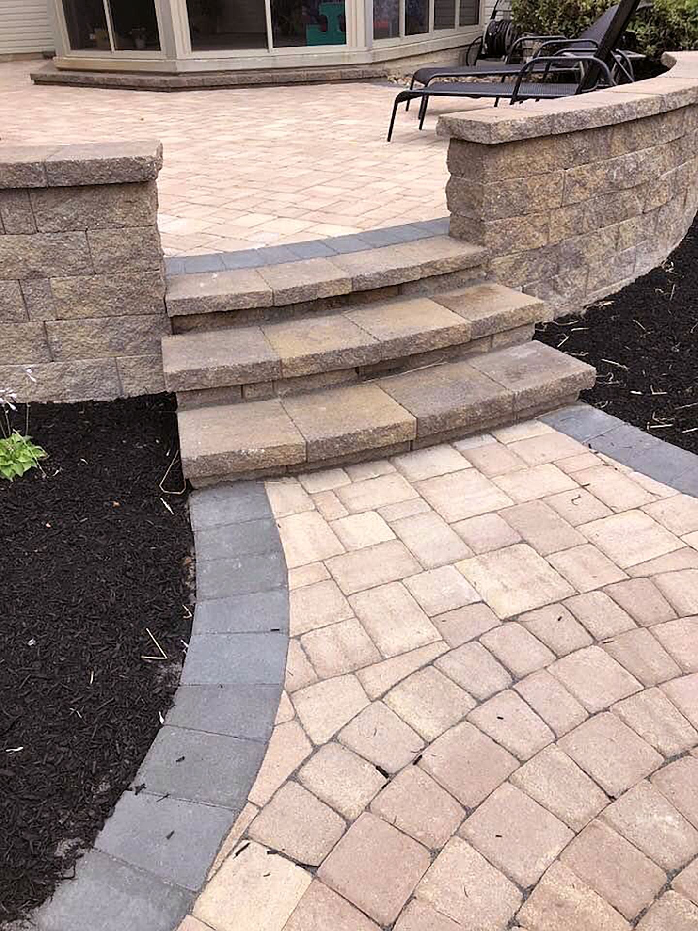 A brick walkway with stairs leading up to a patio.